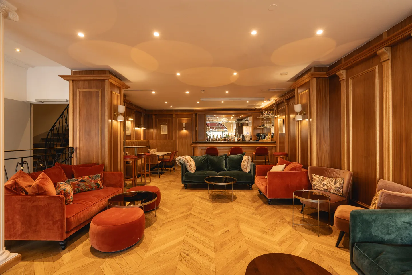 The bar salon: rust and green velvet sofas on herringbone parquet, the counter beyond