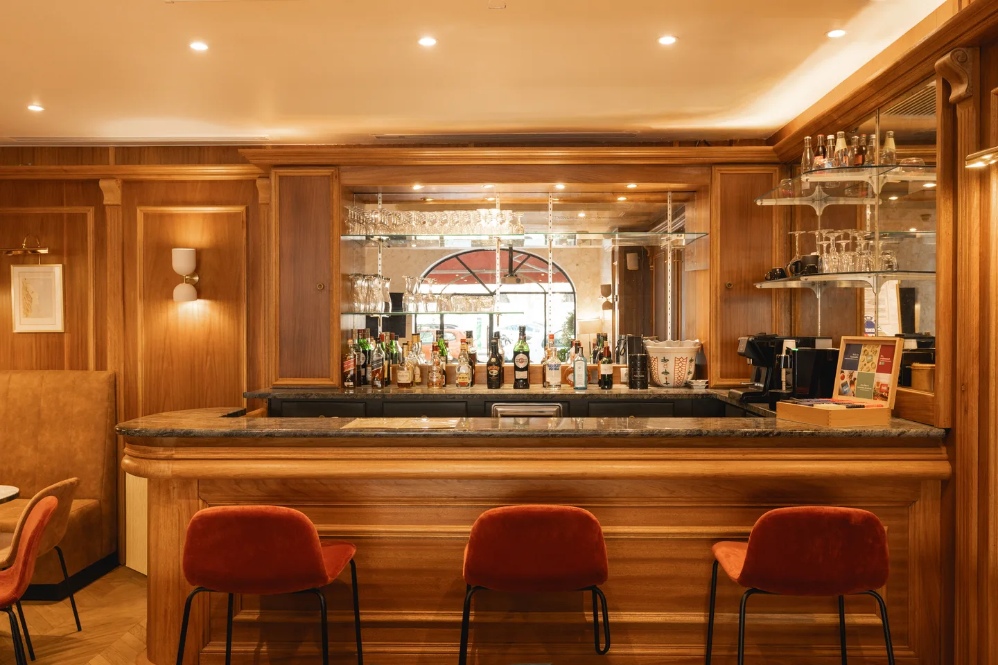 The bar counter: marble top, rust velvet stools and a mirrored back-bar in wood panelling